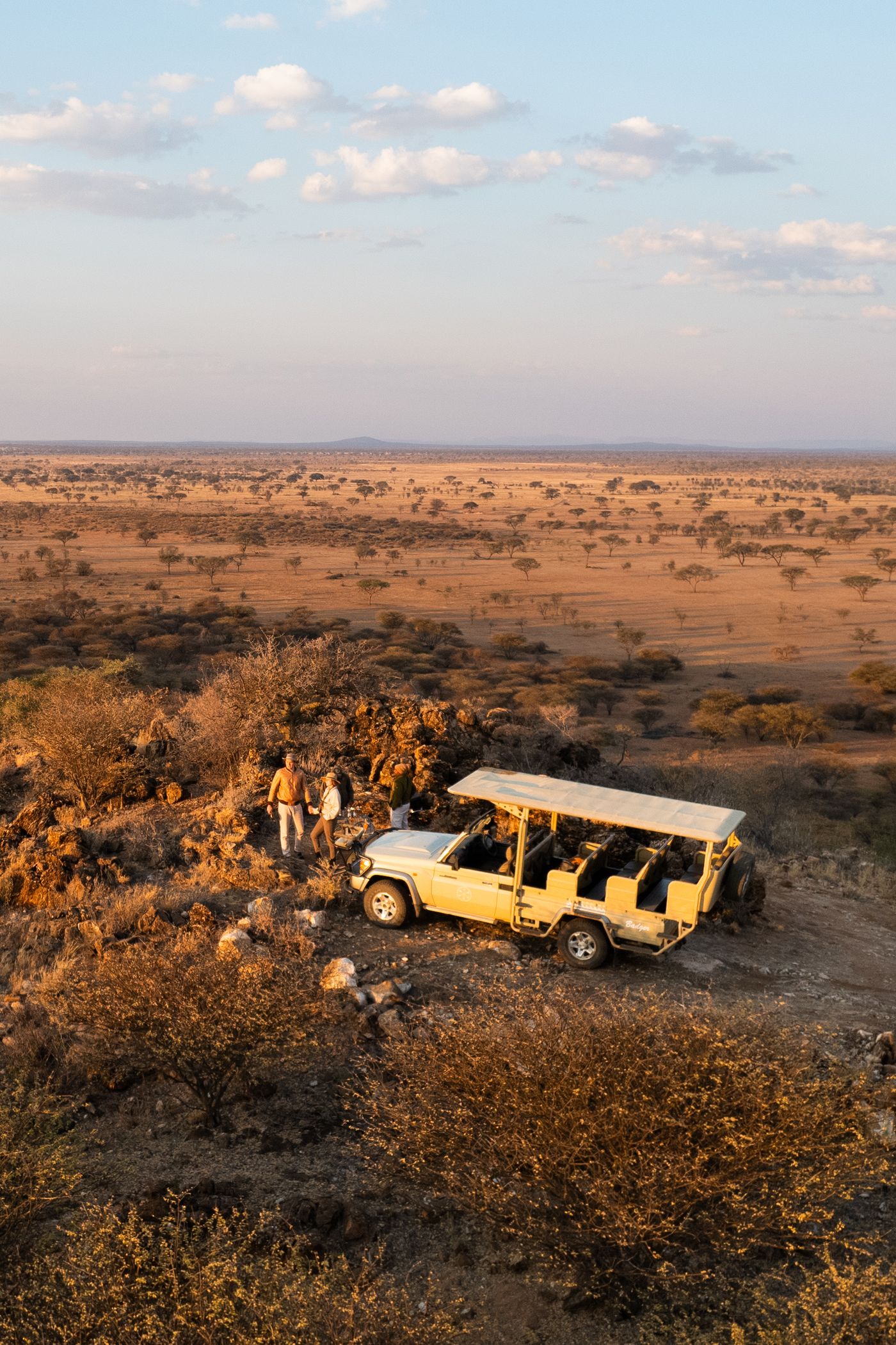 An open-sided safari jeep with two passengers driving through the African savannah in Namibia at sunset