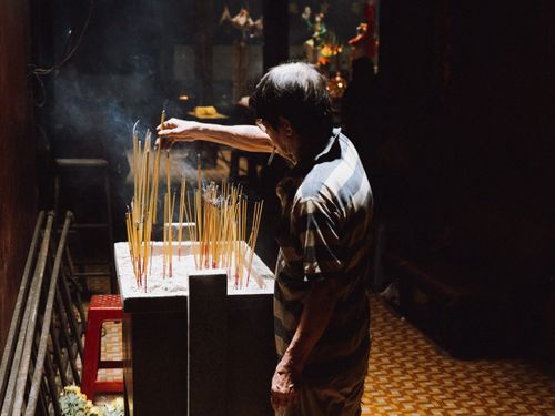 Free A man in a dark setting carefully lights incense sticks in a temple, creating a spiritual and serene atmosphere. Stock Photo