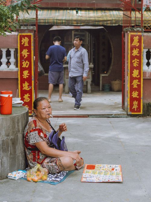 Free A street vendor sits by a Chinese temple entrance surrounded by colorful items and visitors. Stock Photo