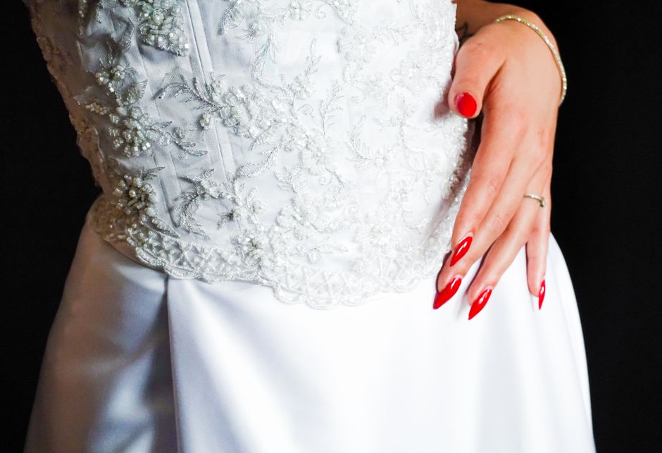 Close-up of elegant white lace wedding dress with intricate patterns and red nails.
