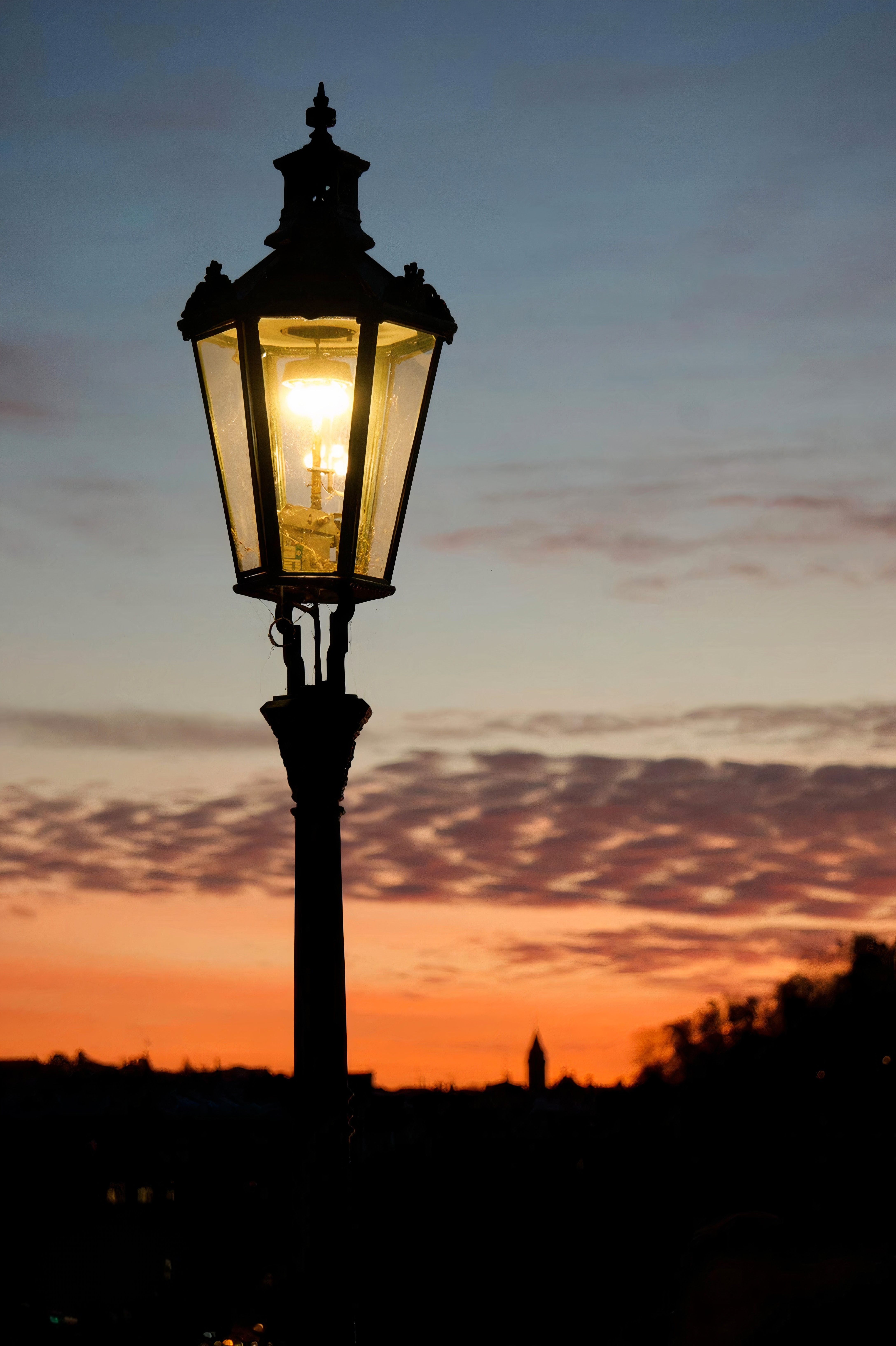 Fotomural Una lámpara de calle clásica que brilla cálidamente contra un cielo crepuscular vívido, creando una escena urbana serena.