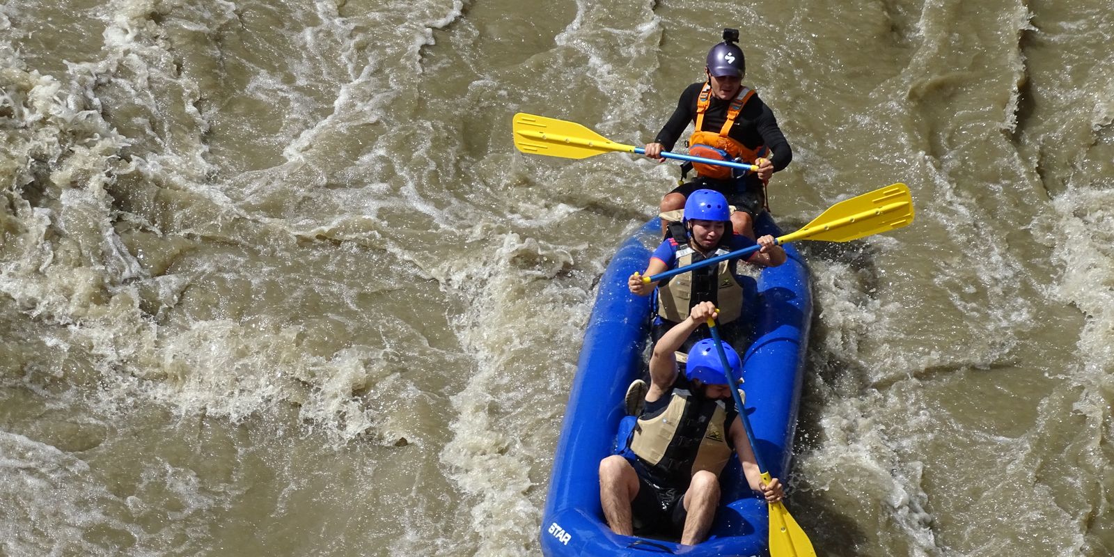 Three rafters navigating rapid waters in an inflatable boat