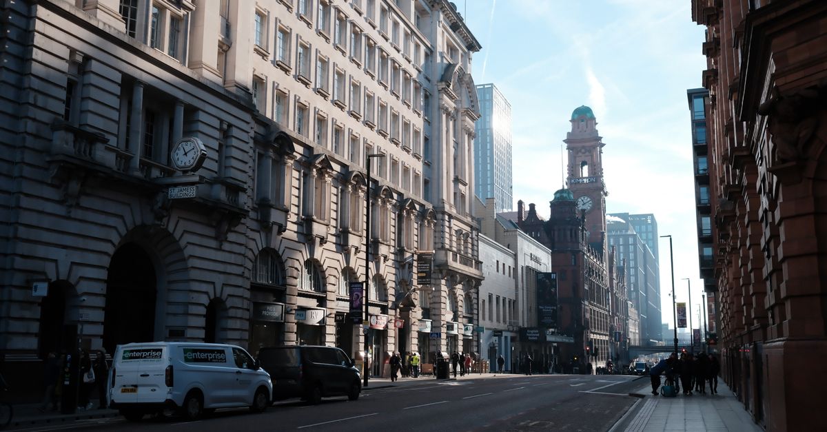 A bustling street in Manchester showcasing historic architecture and urban life on a sunny day.