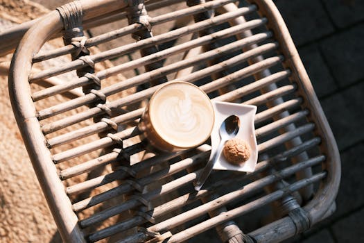 Top-down view of a latte with beautiful art and a biscotti on a wicker table in natural light.