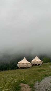 Two luxury tents on a foggy hillside offer a serene camping experience amid lush greenery.