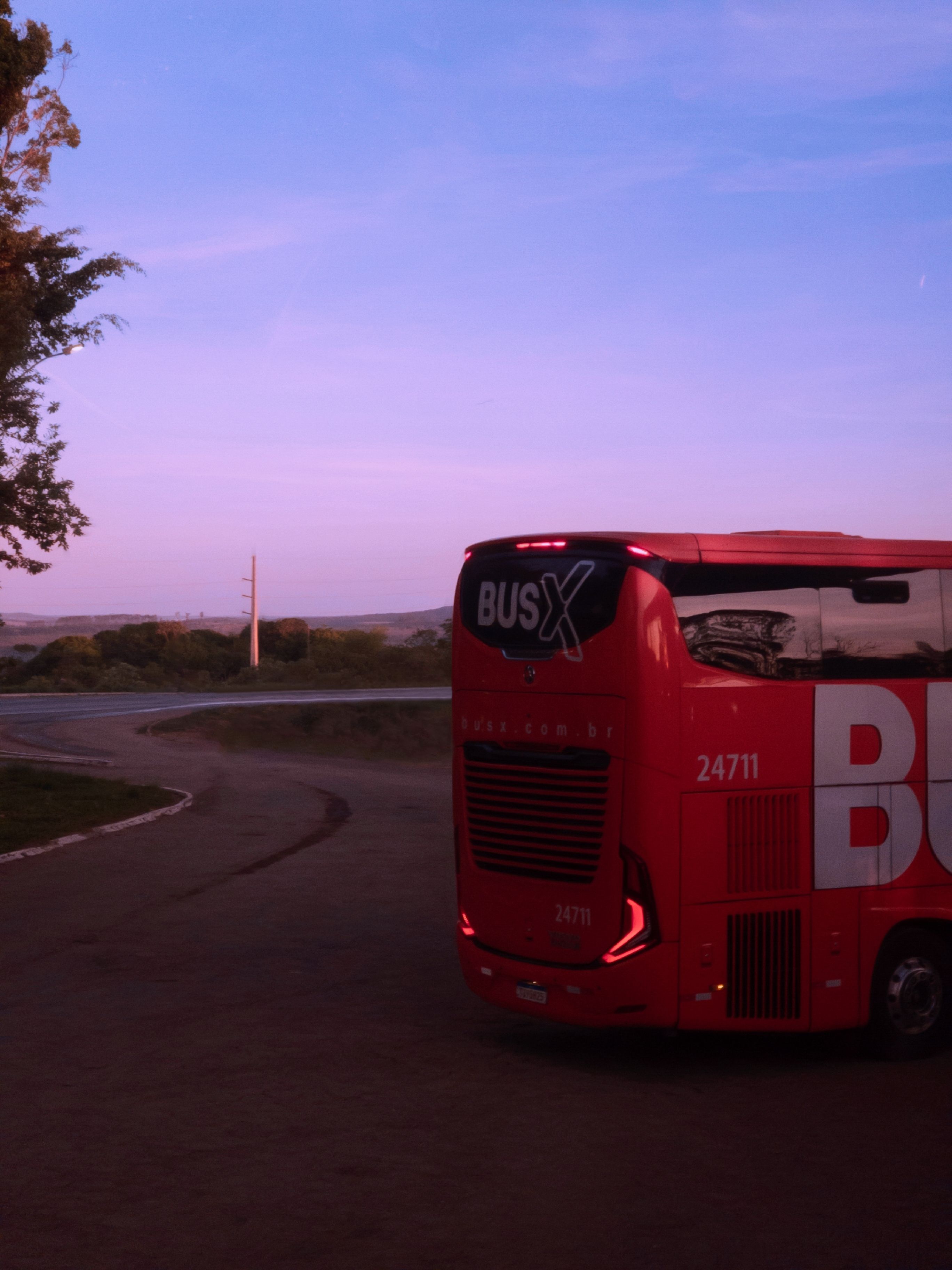 A red bus on a road in Cristalina, Brazil, captured at sunrise with a vivid sky backdrop.