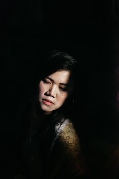 一幅东亚女性的艺术肖像，戏剧性的灯光突显了其情感深度