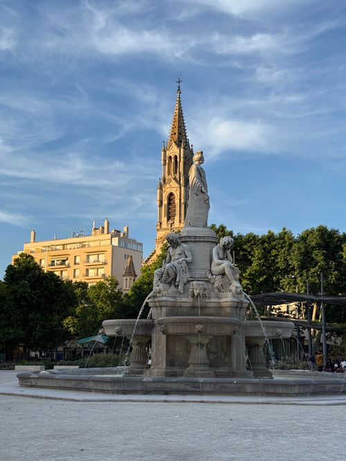 Free Charming view of a historic French fountain with a church tower in the background. Stock Photo