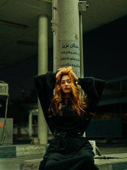 Moody portrait of a woman with long red hair at a gas station at night.