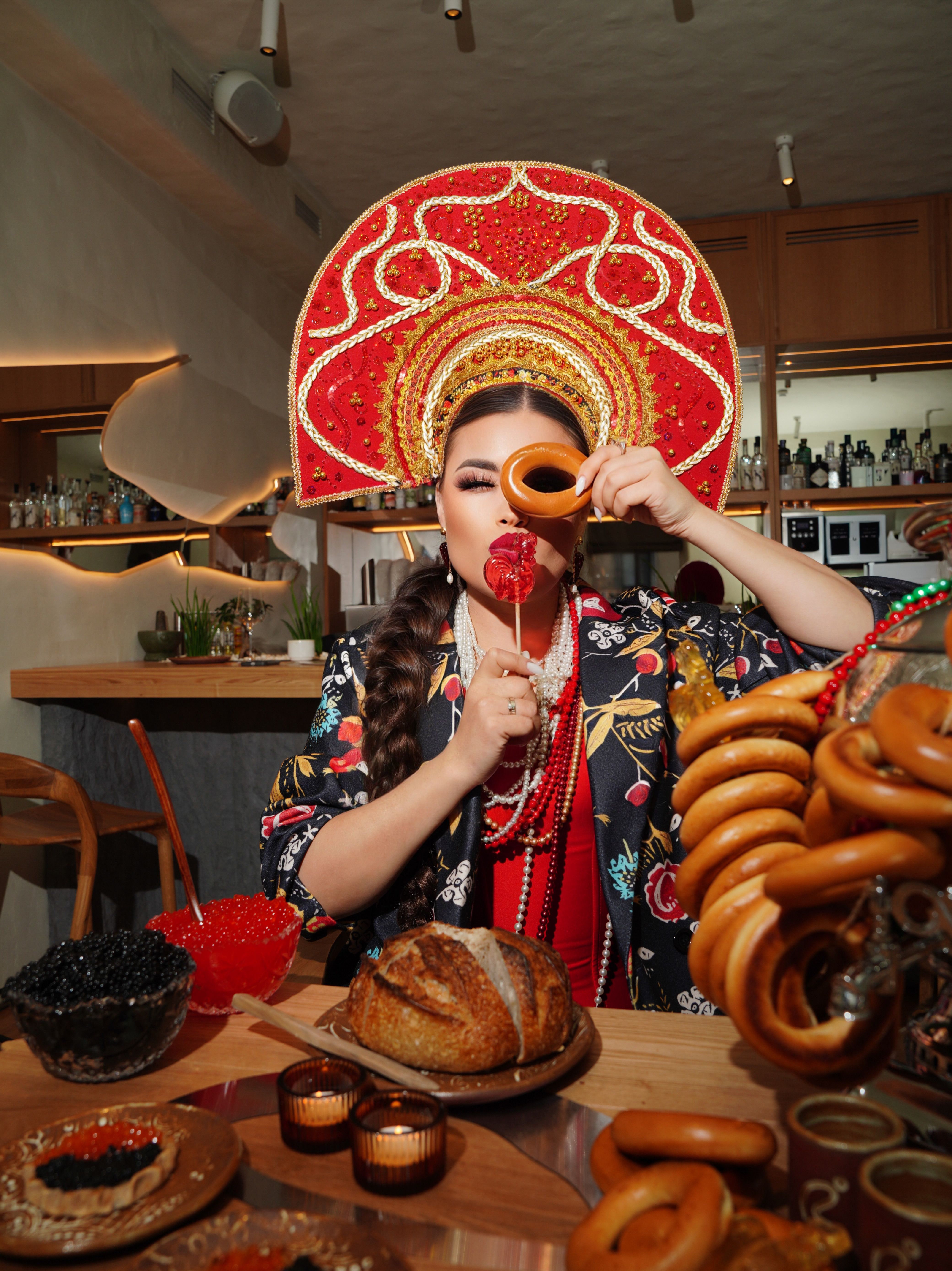 Woman in Russian costume at a cafe table with bread and traditional treats.