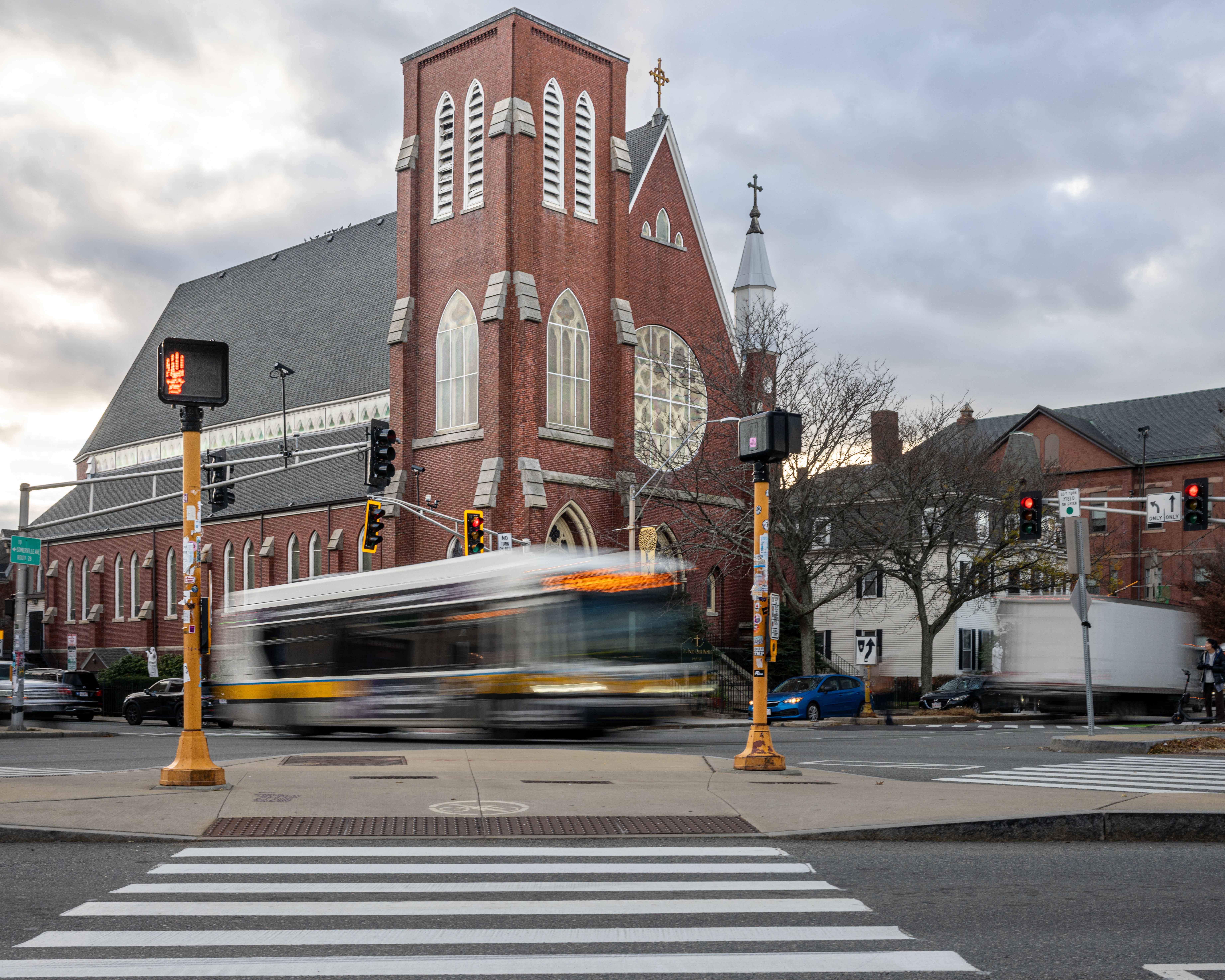 Brick church with moving bus at a busy Somerville intersection during the day.