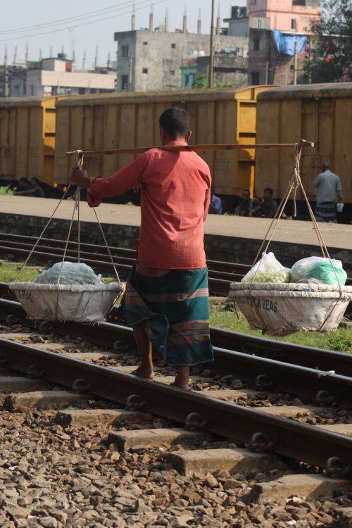Free A vendor balances goods in baskets while walking along railway tracks. Stock Photo