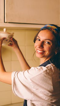 A cheerful woman in a retro kitchen reaches for a teapot, wearing a vibrant headscarf.