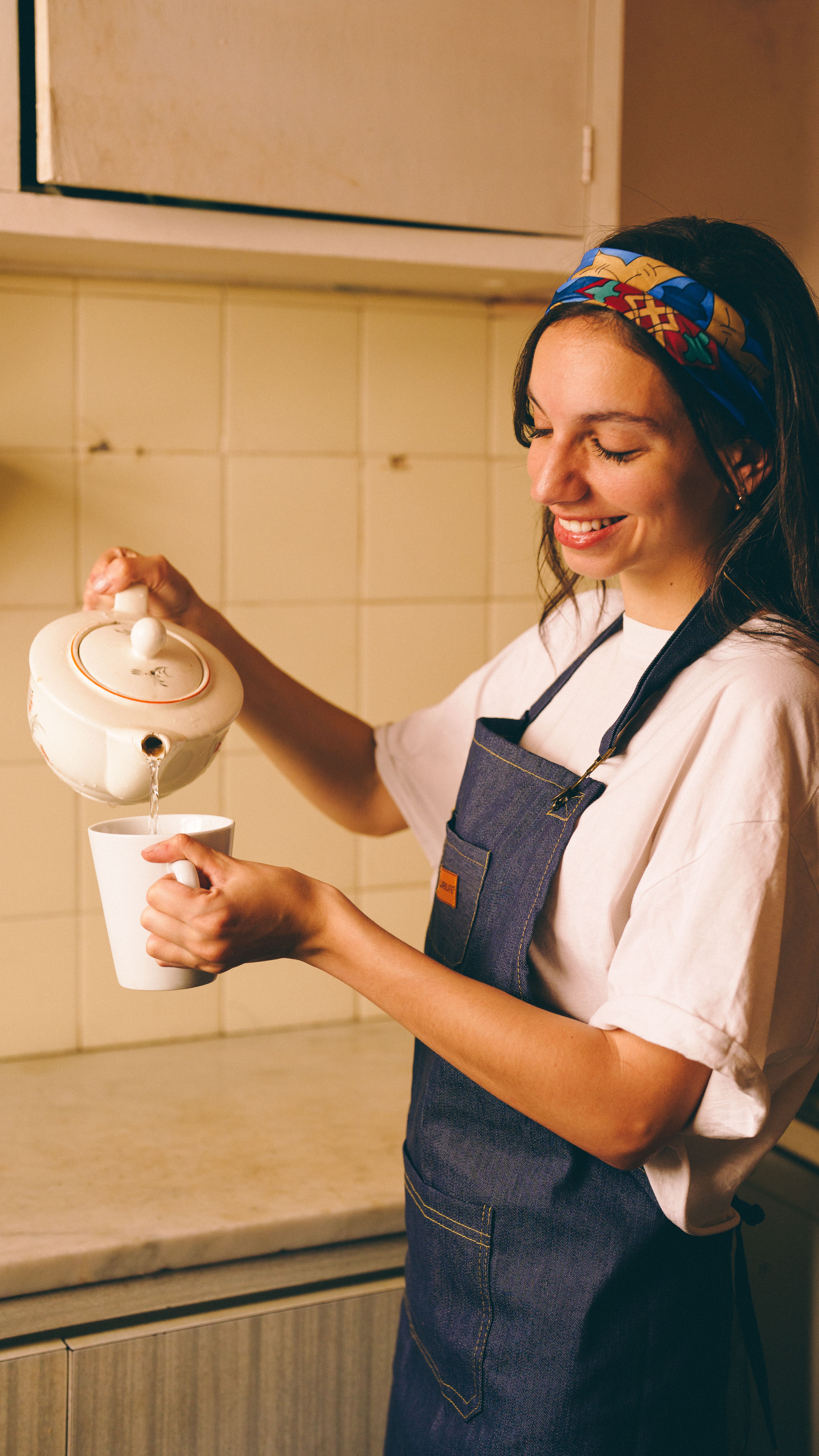 Young woman in apron pouring tea in a cozy kitchen. Warm atmosphere.