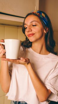 Smiling woman in casual white shirt holding a coffee mug indoors.