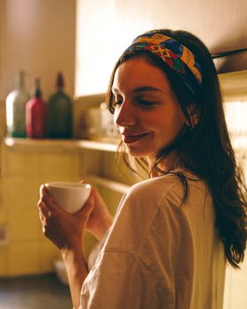 A young woman savors her morning coffee in a warm, sunlit kitchen setting.