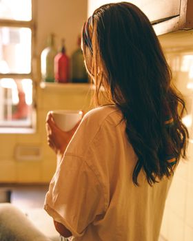 Cozy morning scene with woman holding coffee in a bright kitchen.