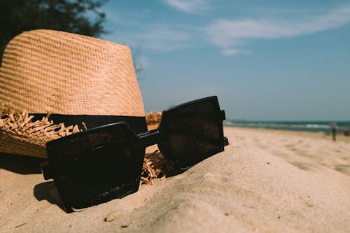 Солнцезащитные очки рядом с шляпой от солнца на песке