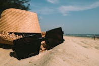 在阳光明媚的日子里，沙滩上摆放着太阳镜和草帽，以海洋为背景，非常适合夏季放松的氛围