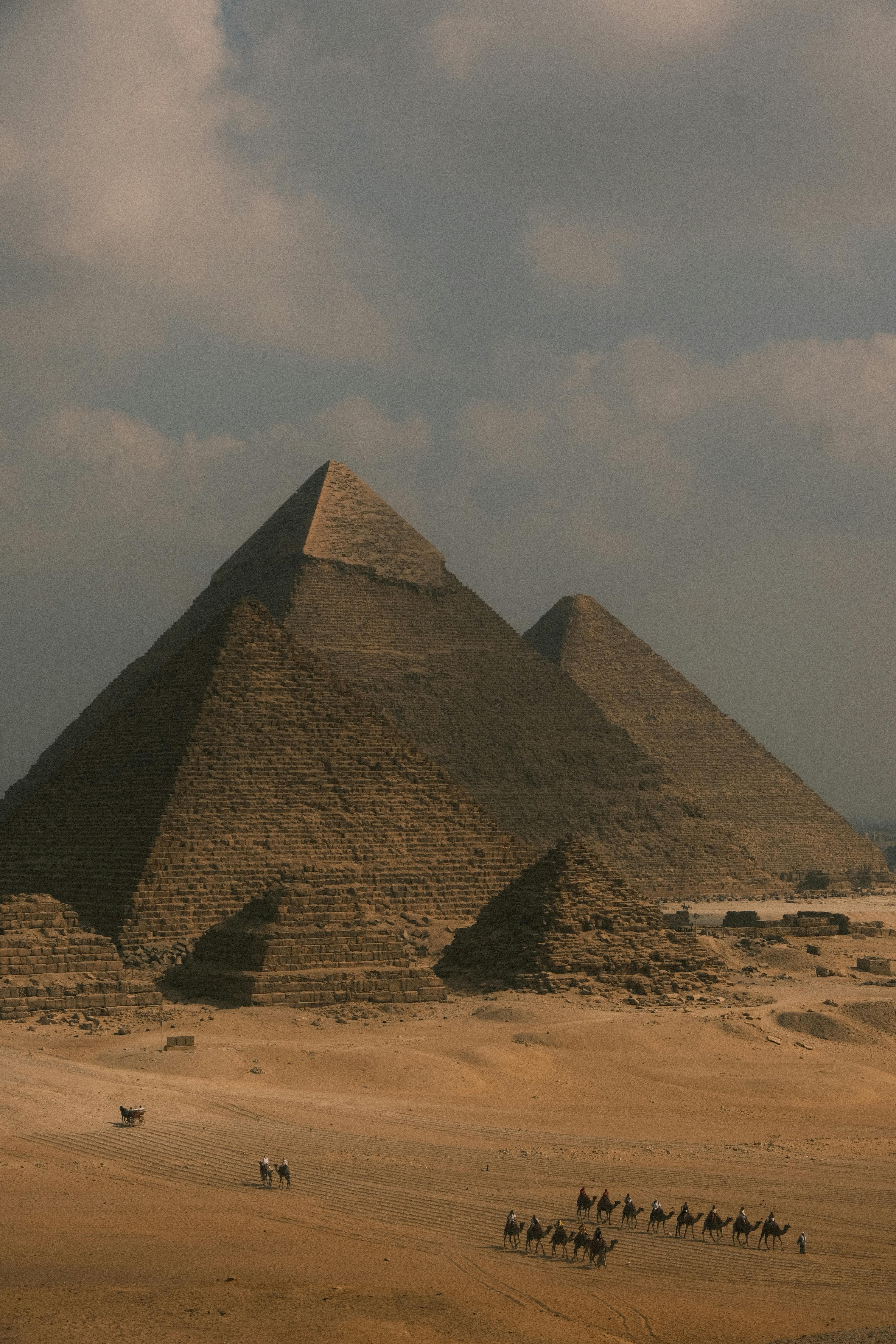 Pyramides de Gizeh avec caravane de chameaux dans le désert sous un ciel nuageux