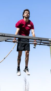 Athletic man in a red shirt performing a pull-up outdoors on a bright sunny day.