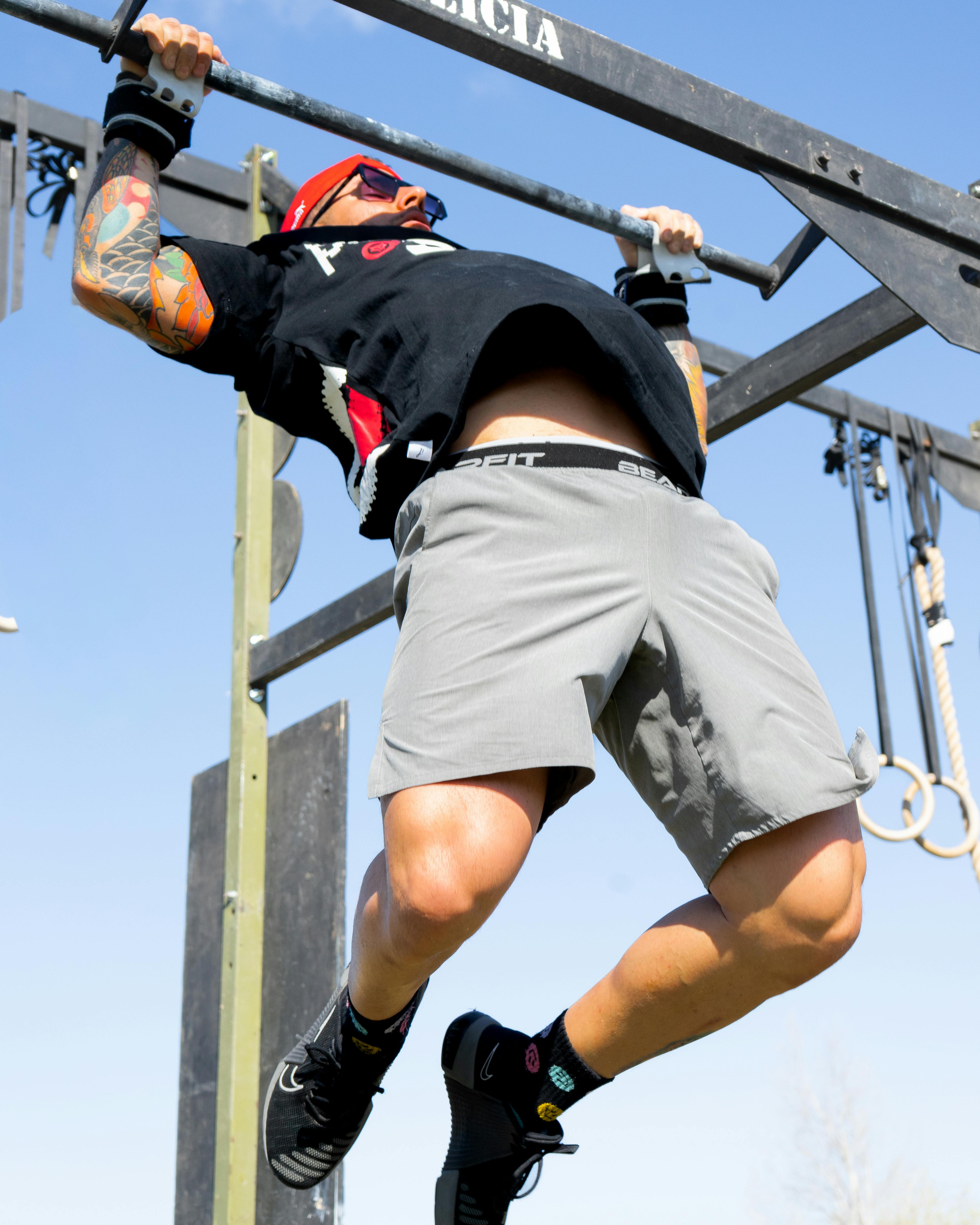 Athletic individual in shorts and cap doing pull-up on a sunny day outdoors.