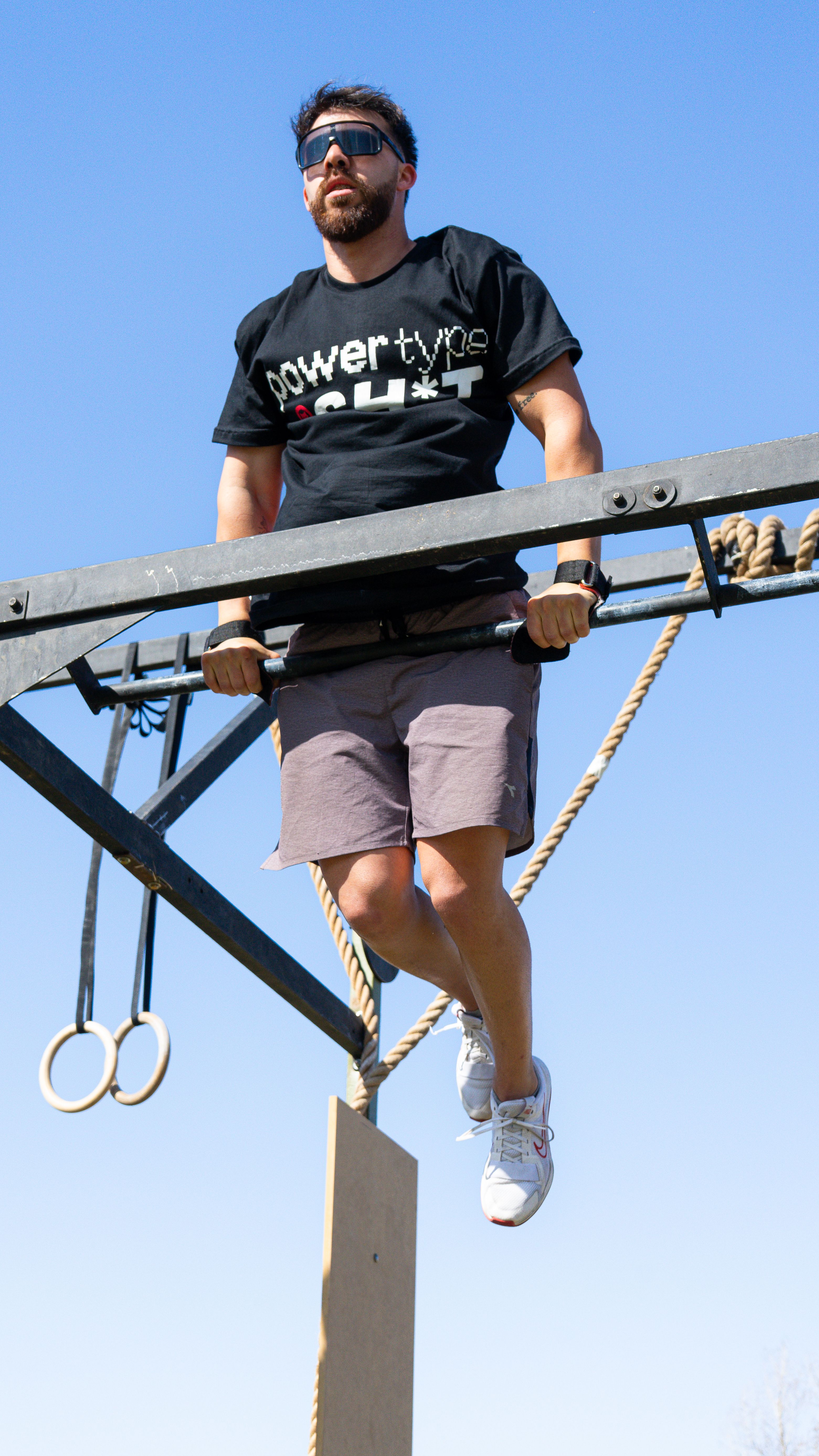 Athletic man doing a pull-up on an outdoor obstacle course under blue sky.