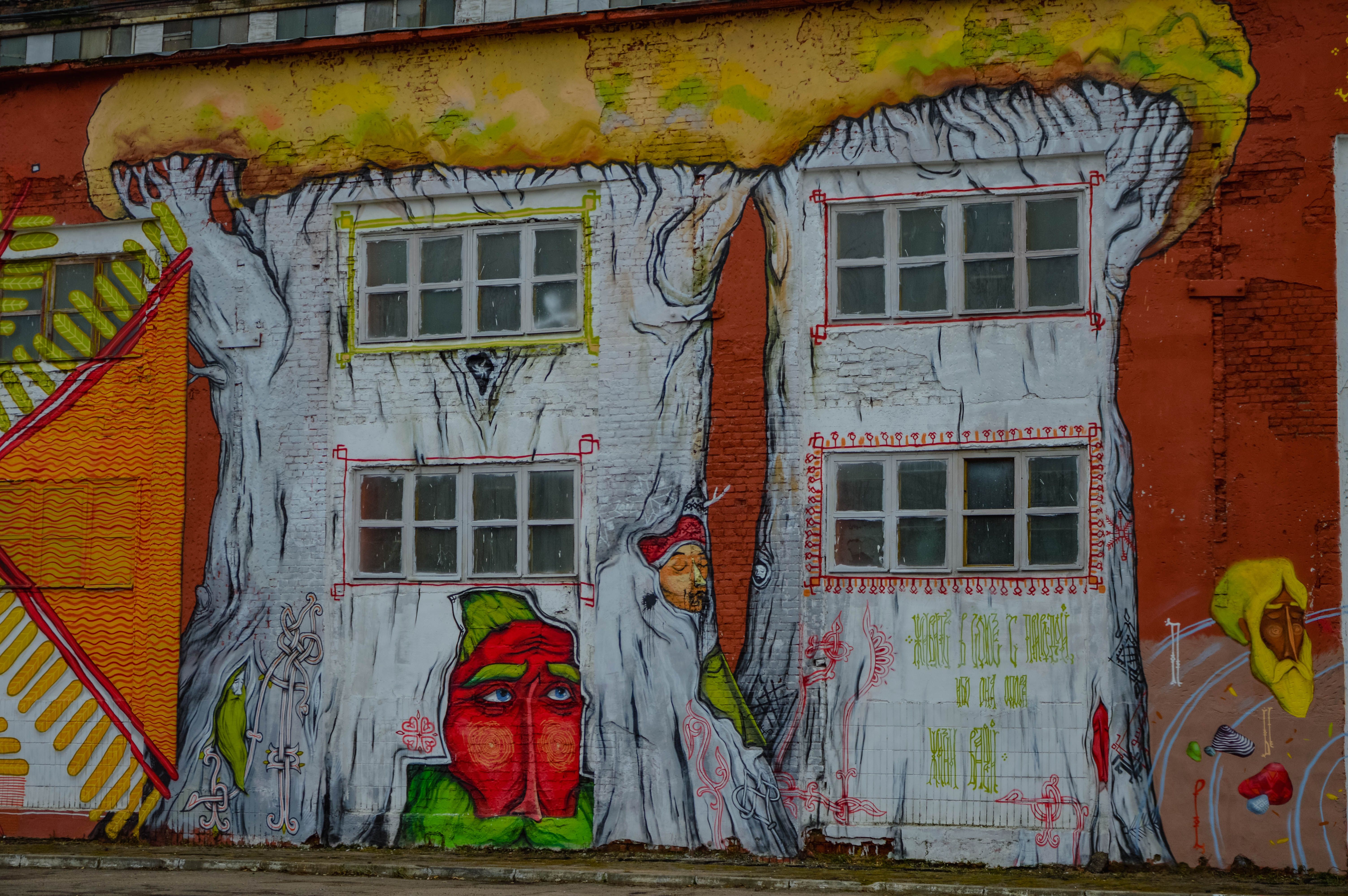 Colorful urban mural depicting fantastical tree designs on a brick building wall, showcasing street art creativity.