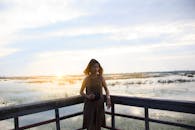 一名年轻女子手持相机，站在木甲板上俯瞰日落时风景优美的湖泊