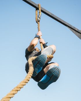 Adult male engaged in outdoor rope climbing exercise during the day for fitness training.