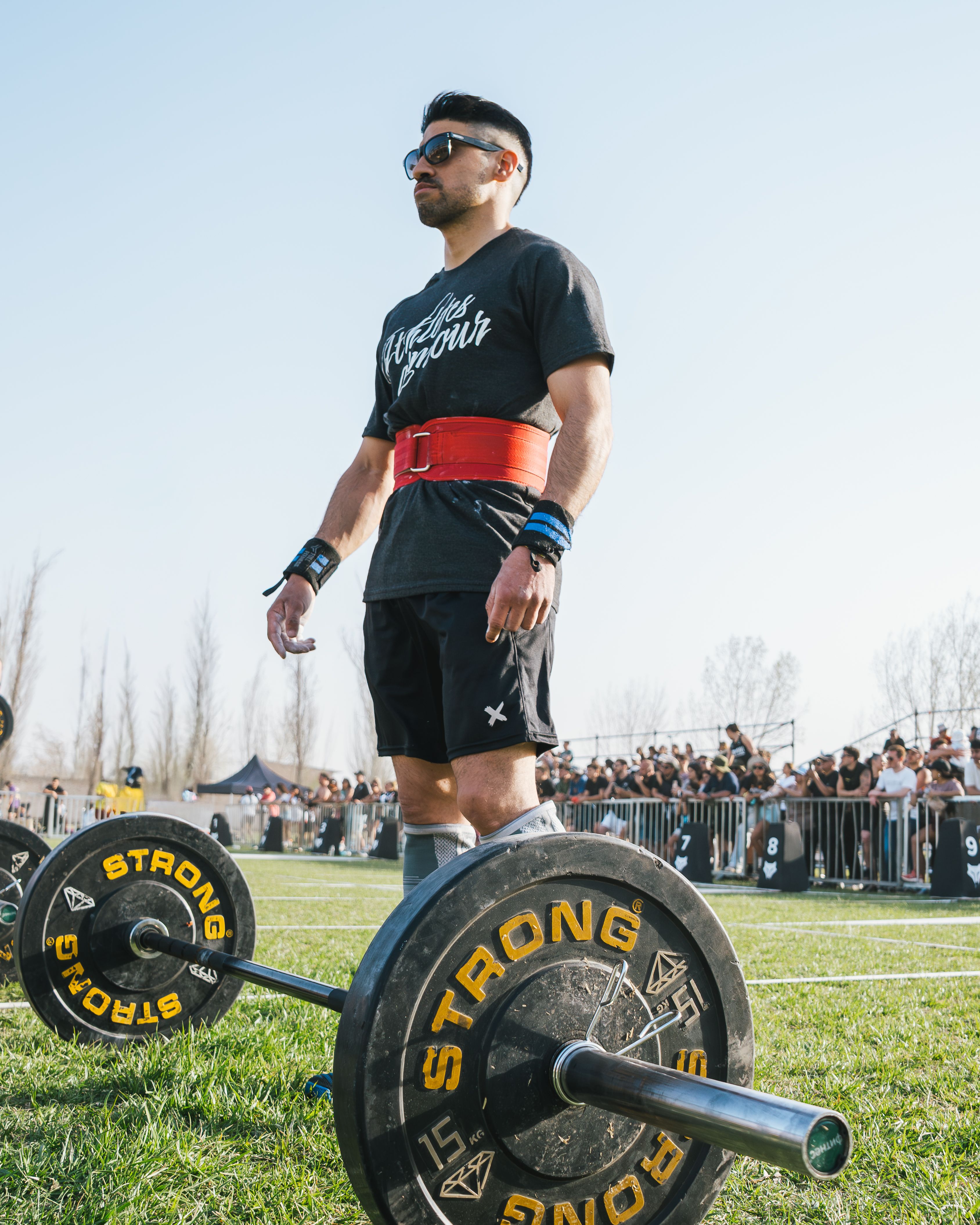 Athlete wearing a red lifting belt preparing for a deadlift at an outdoor competition