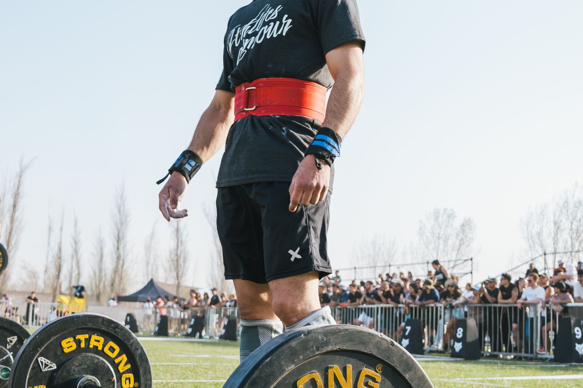 Athlete wearing a red lifting belt preparing for a deadlift at an outdoor competition