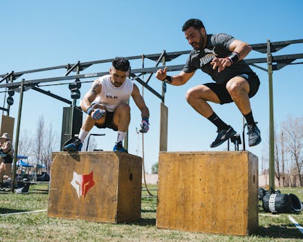 Two men demonstrating intense box jump exercises at an outdoor fitness event.