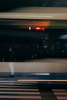 A dynamic night shot capturing city life with a pedestrian and blurred bus movement.