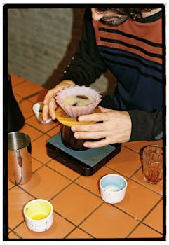 Person brewing coffee using a pour-over method on a tiled counter.