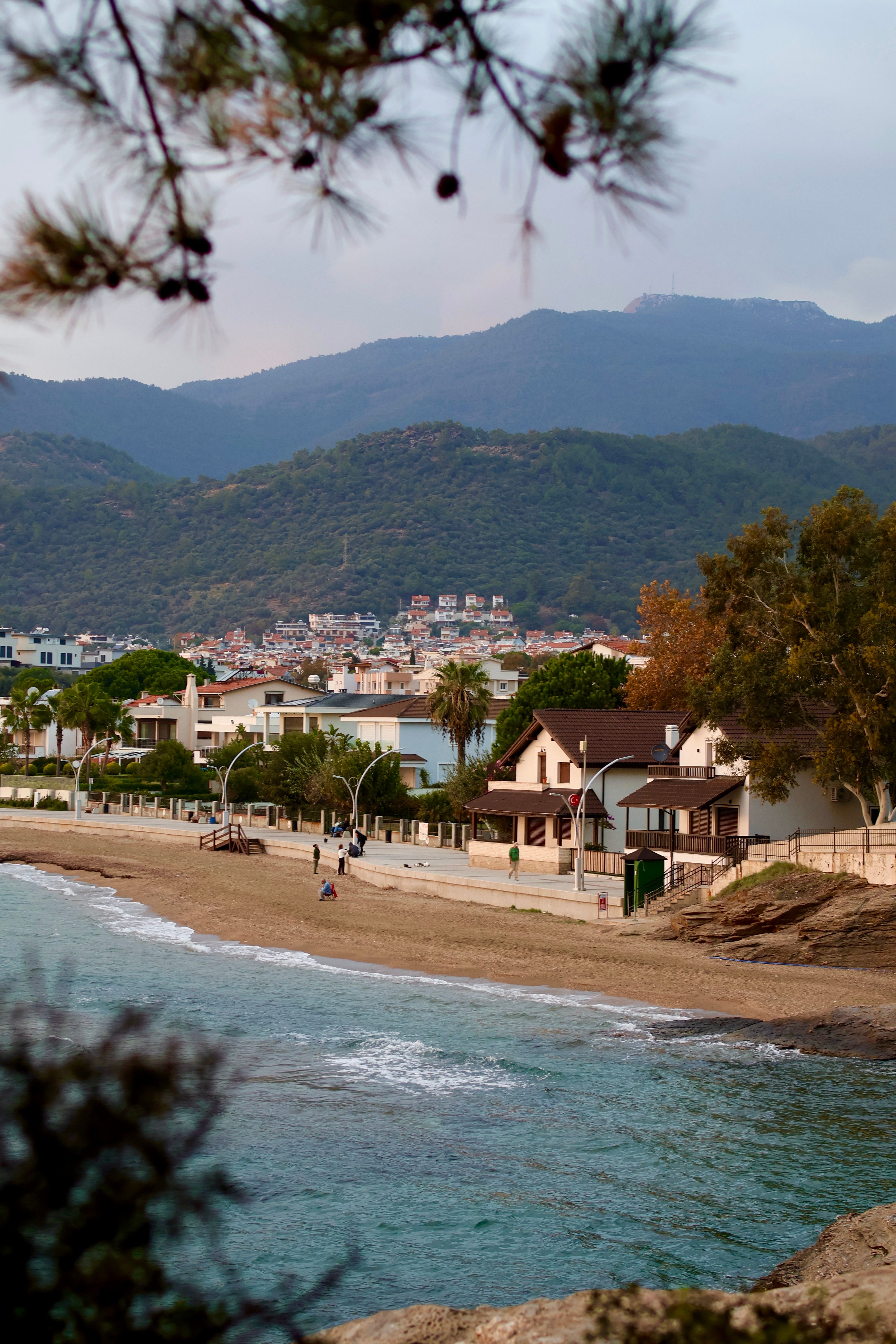 Coastal village with beach, houses, and mountains in the background during a serene day.