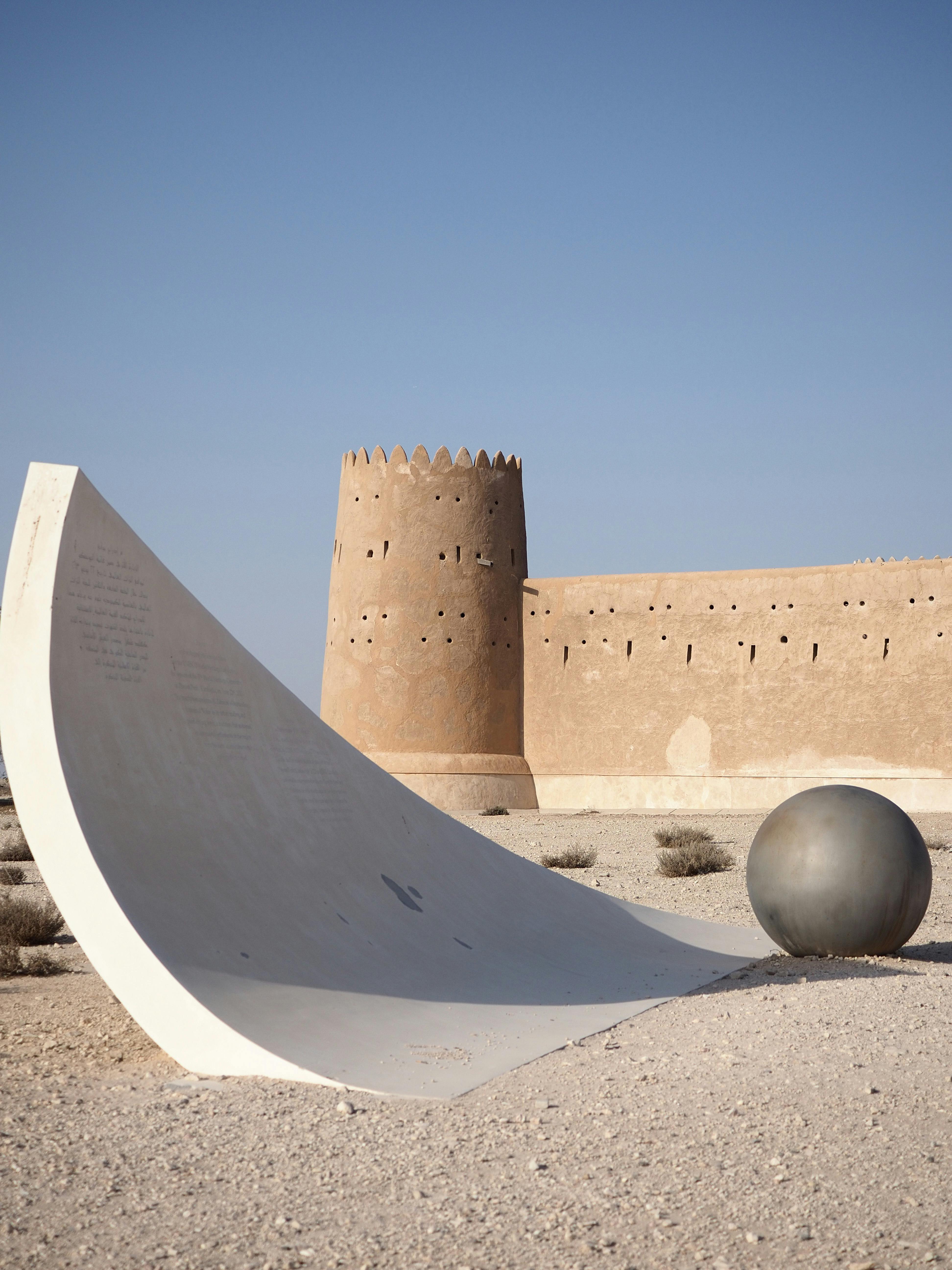 Ancient fort in the Qatari desert with modern art installation under clear skies.