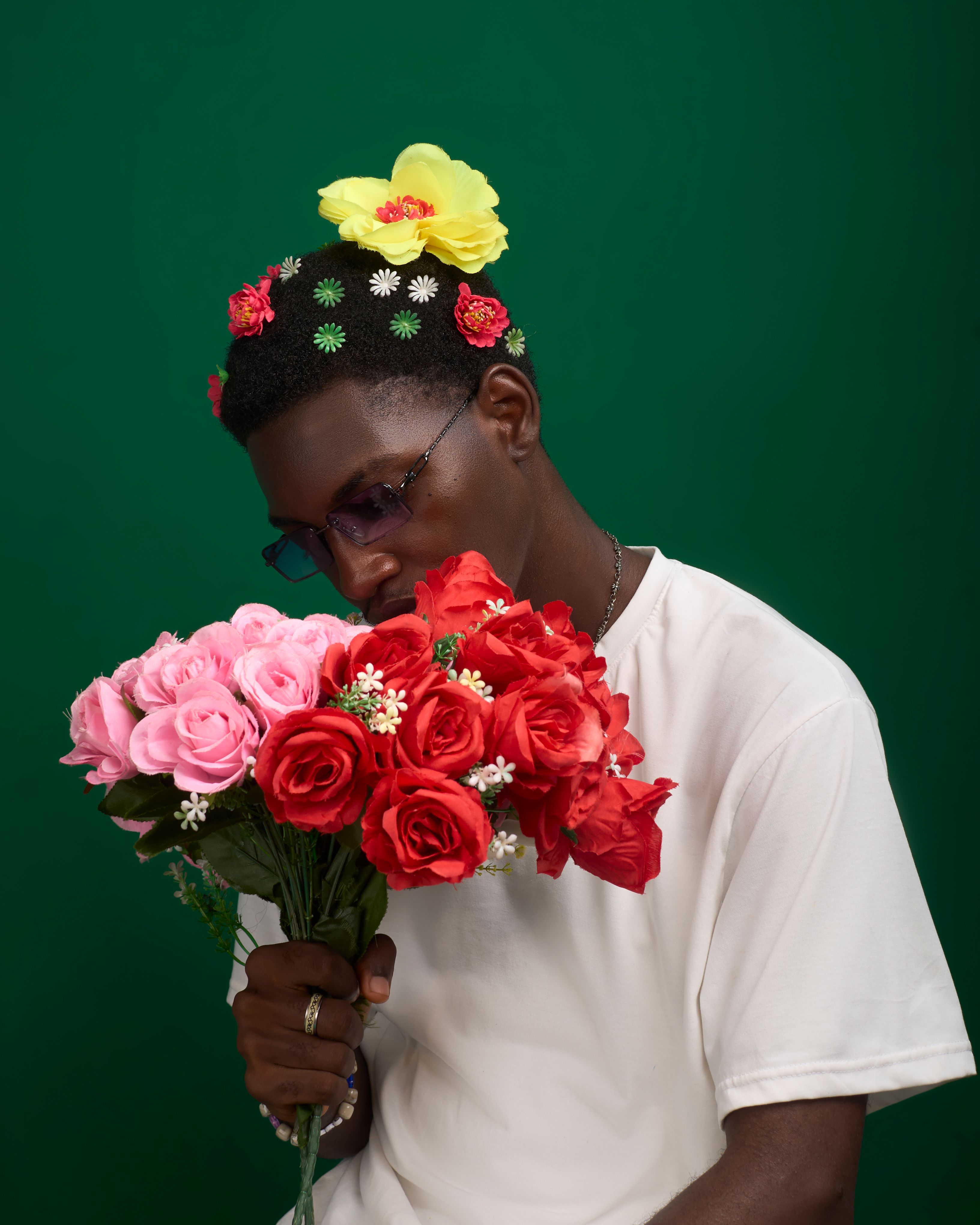A stylish man holding vibrant roses against a green background, showcasing floral fashion.
