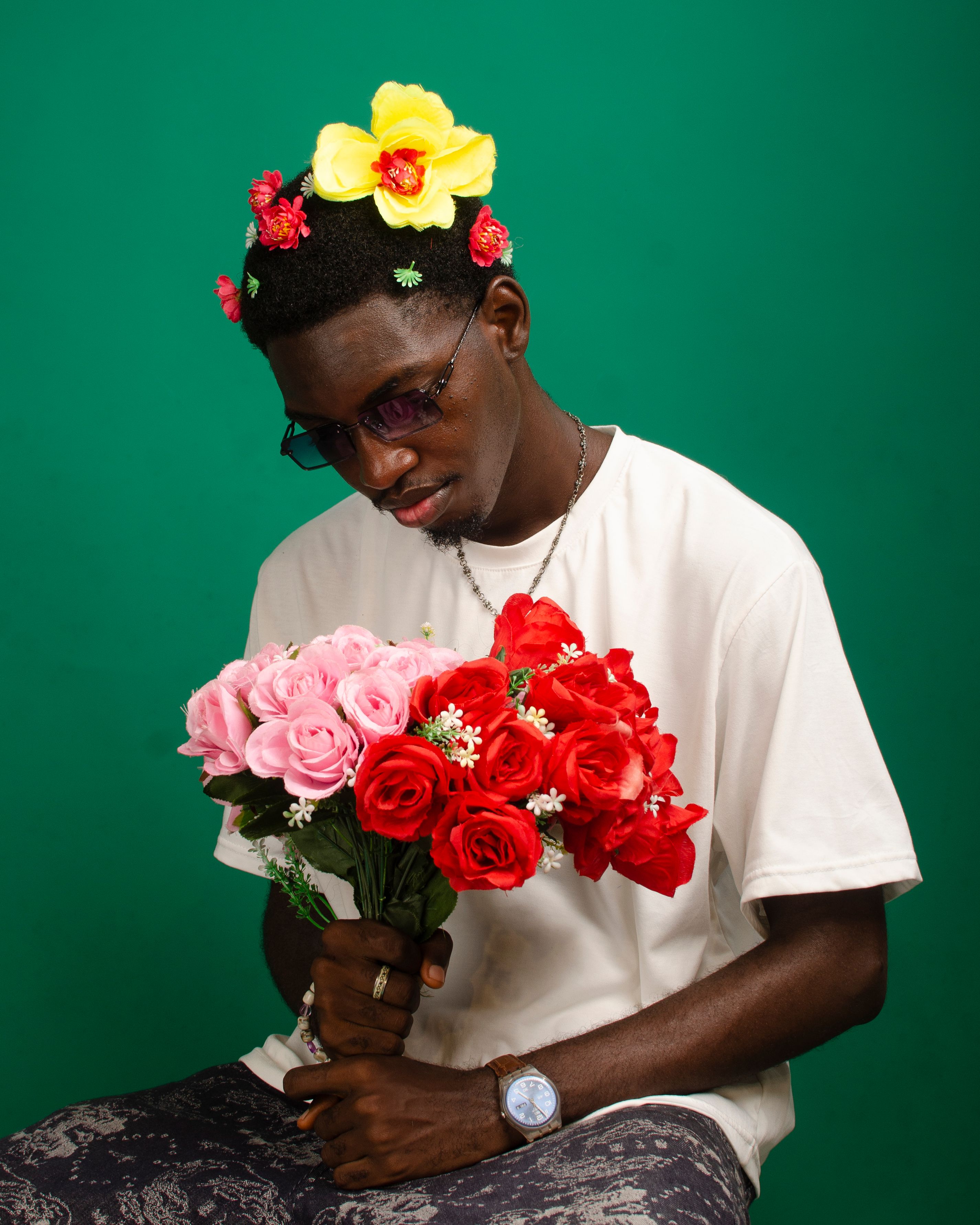 A fashionable adult wearing floral accessories and sunglasses, holding vibrant roses against a green backdrop.