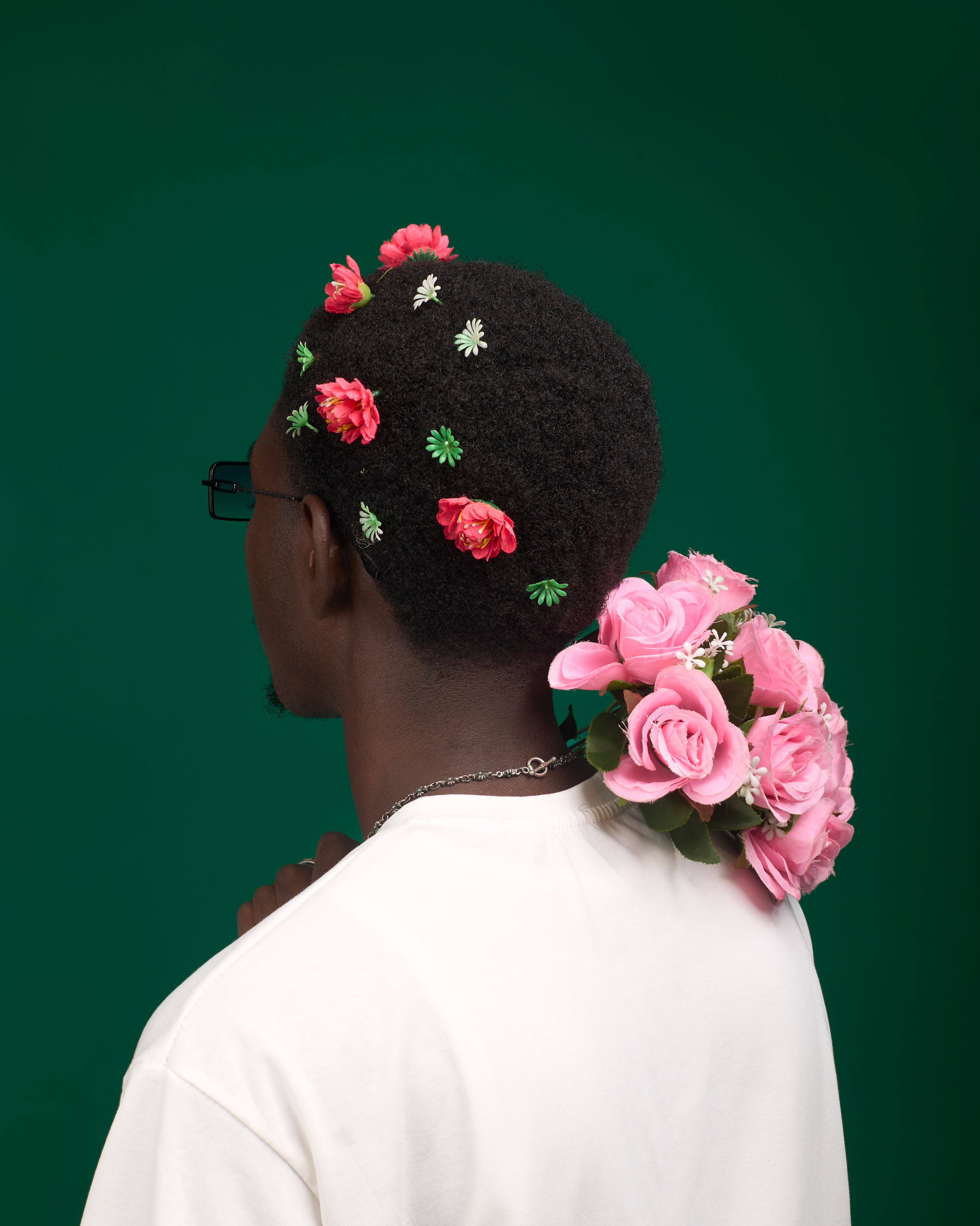 A creative portrait featuring a man adorned with vibrant flowers against a green background, evoking a sense of nature and art.