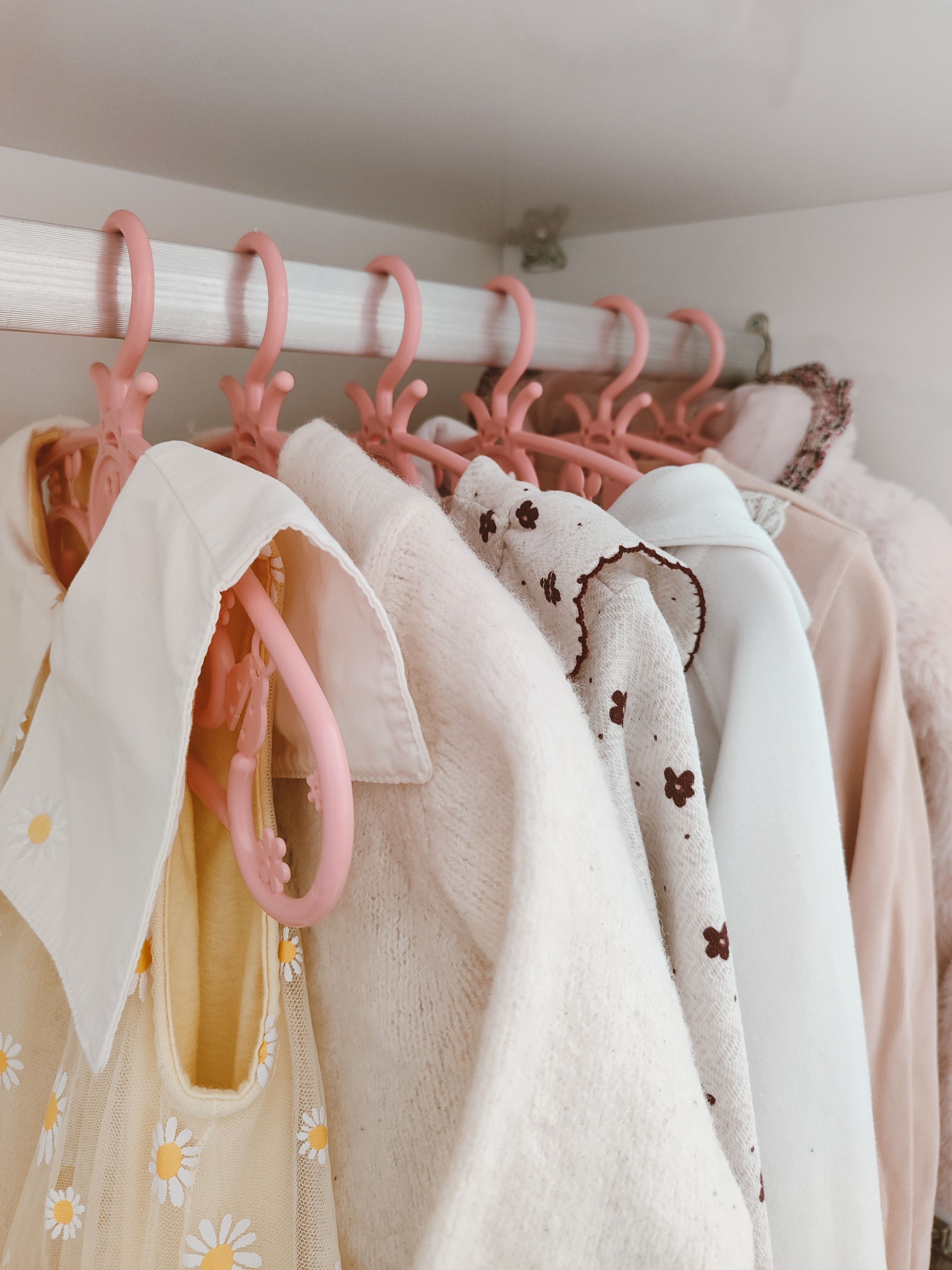 Cozy pastel clothes neatly arranged on pink hangers in a closet.