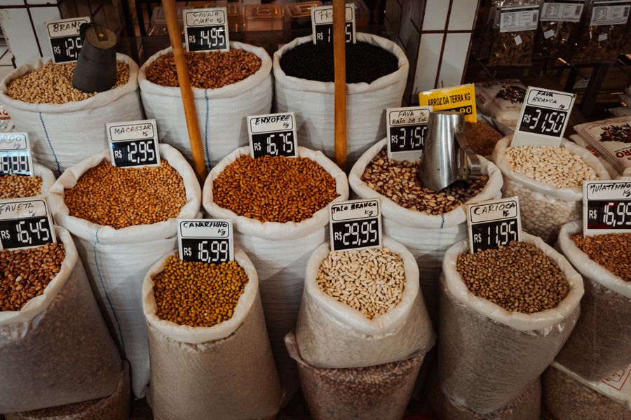 Colorful market display of various beans in large sacks with price tags.