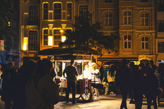 A bustling evening scene with a street vendor illuminated by warm light in a city square.