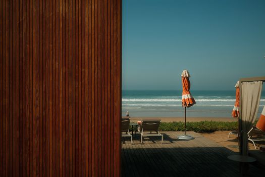Peaceful beachfront setting in Morocco with deck chairs and closed orange umbrellas, perfect for relaxation.