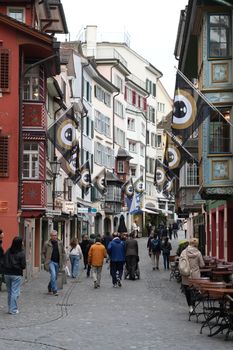 Busy street in Zurich, featuring colorful buildings and vibrant flags, capturing local architecture and daily life.