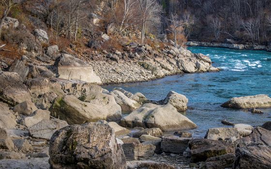 Autumn landscape with rocky riverbank and turquoise flowing river.