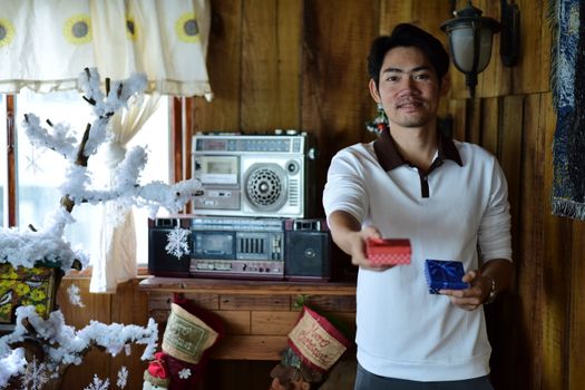 A man offers gifts in a warm, rustic room with vintage decor and festive holiday elements.