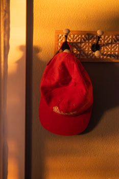 A vibrant red cap hangs indoors, illuminated by the warm glow of sunset, creating a cozy atmosphere.