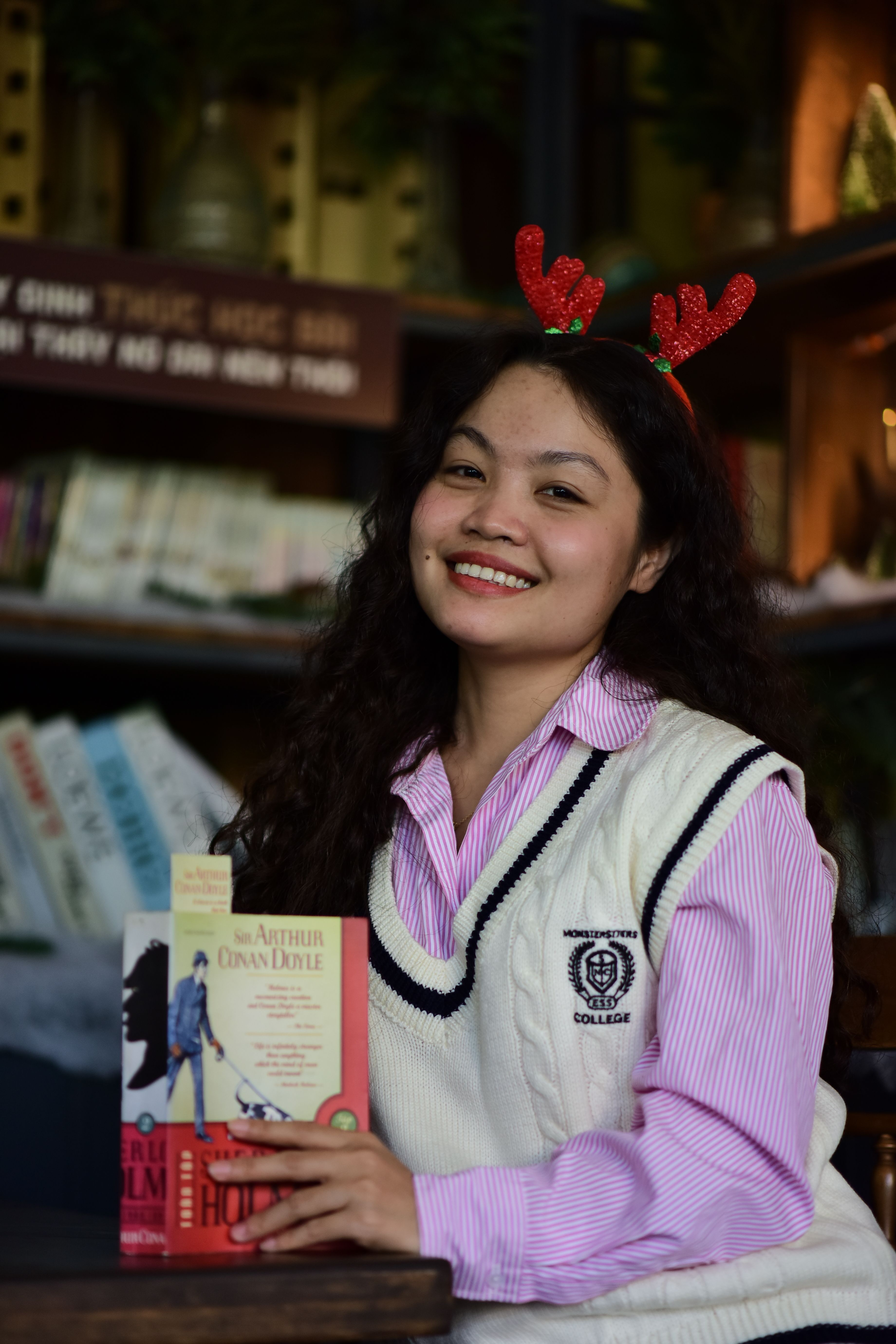 Smiling woman with reindeer antlers holding a book in a cozy indoor setting.