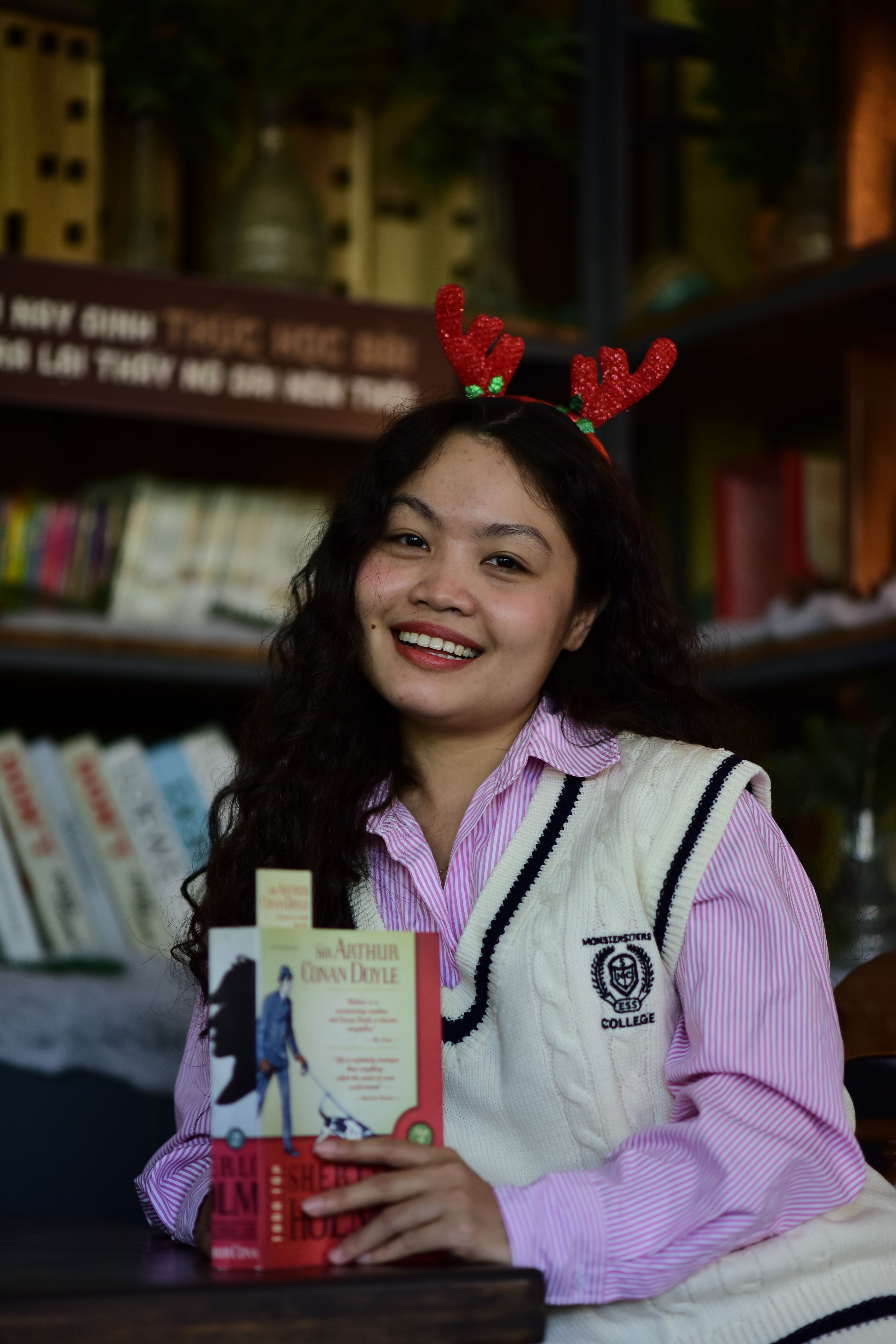 Smiling woman in a bookstore with festive reindeer headband and books by Arthur Conan Doyle.